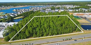 A large wooded plot of land outlined near a busy road and residential area.