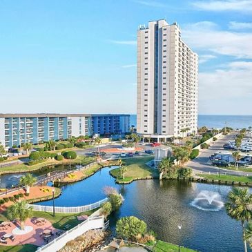 Coastal resort with tall buildings, a pond, and a parking area near the ocean.