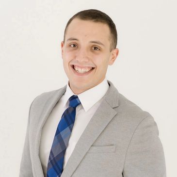 Smiling man in a gray suit with a blue plaid tie against a white background.