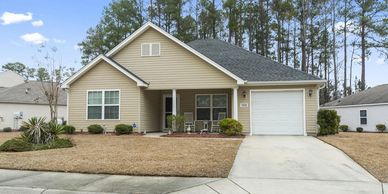 Single-story beige house with a garage and front porch in a suburban neighborhood.