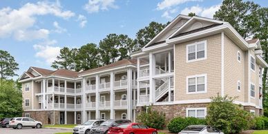 Modern apartment complex with multiple cars parked outside on a clear day.