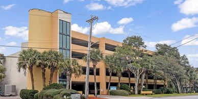 A multi-story parking garage surrounded by palm trees and greenery on a sunny day.