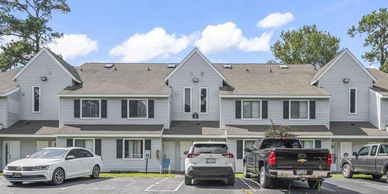 Row of modern townhouses with parked vehicles under a blue sky.