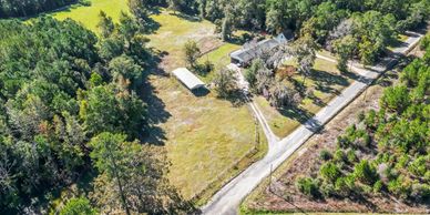 A rural property with a house, a shed, and surrounding trees near a curved road.