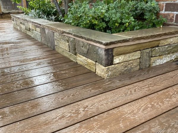 Stonework flowerbed next to artificial decking. Stone mason, Decking installer