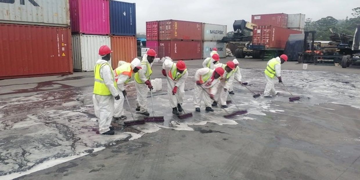 Workers cleaning an industrial area with brooms and protective gear.