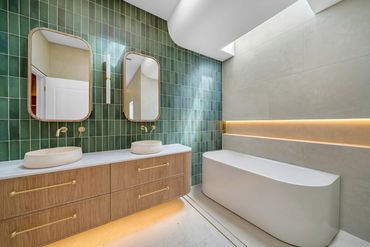 Modern bathroom with green tiles, dual mirrors, and a sleek bathtub.