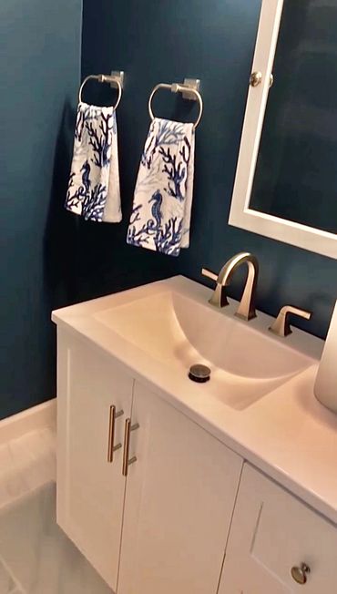 Modern bathroom sink area with navy walls and decorative towels.