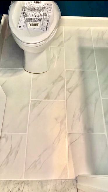 Newly installed white marble tile flooring next to a toilet.