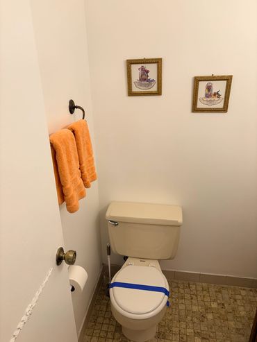 Small bathroom with a closed toilet, orange towels, and framed pictures on the wall.