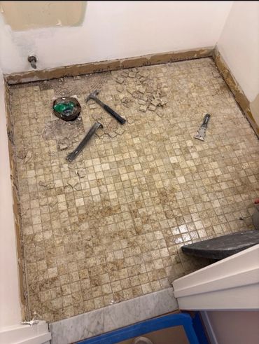 Bathroom floor with old tiles being removed and tools scattered.