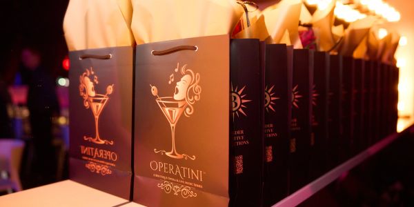 Line of elegant black gift bags with orange designs and orange paper inside.