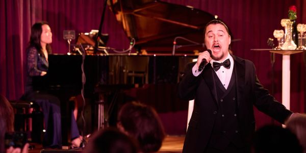 Man singing passionately with pianist in background.