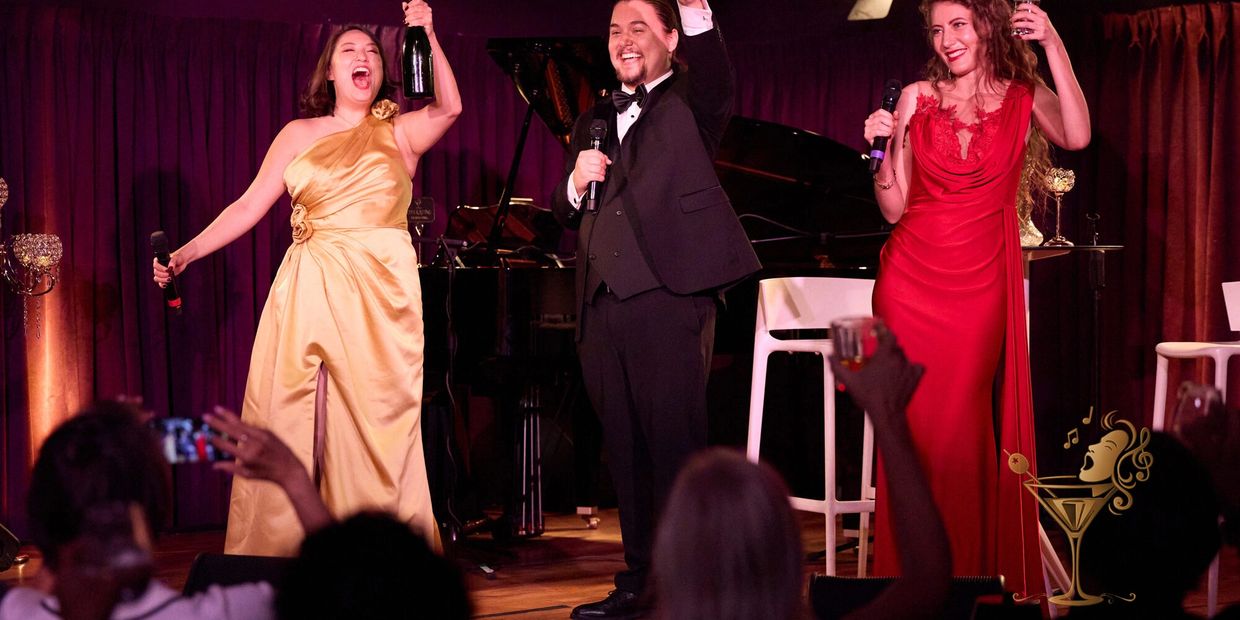 Three people celebrating on stage with drinks and microphones.