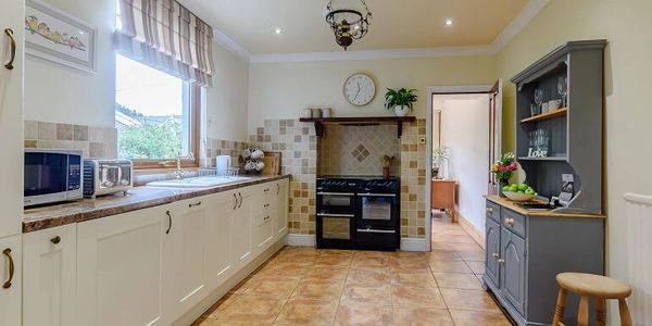 A long row of cream units sit opposite a grey dresser in a bright, spacious kitchen. 