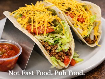 Two loaded tacos with ground beef, lettuce, tomato, jalapeños, and shredded cheese on a plate.