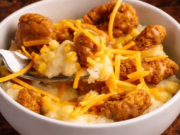 Bowl of cheesy grits topped with fried chicken bites and shredded cheddar cheese.