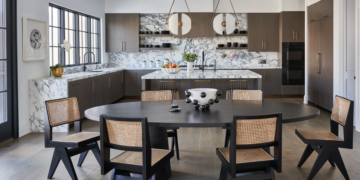 Modern kitchen with marble countertops and unique black chairs around a dark oval table.