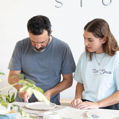 Man teaching woman pottery making in a studio.