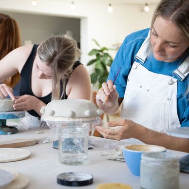 Two women focused on sculpting clay in a pottery class.