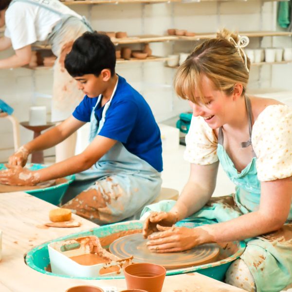 Two children happily shaping clay on potter's wheels in a pottery class.