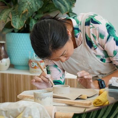 Woman carefully shaping pottery with hands and brush.