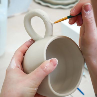 Hands painting details on a ceramic mug handle.