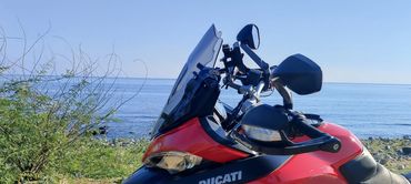 Red Ducati motorcycle parked near a rocky shoreline with ocean views.