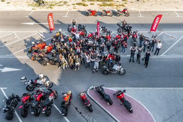 Group of Ducati motorcyclists gathered with their bikes and Ducati flags.