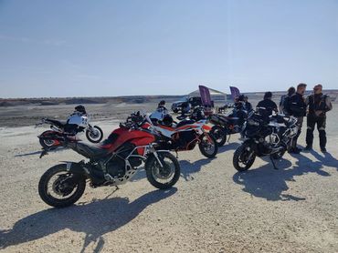 Group of motorcycles and riders gathered on a sunny, open terrain.