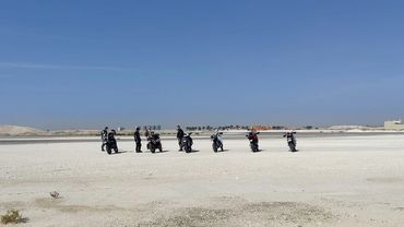 Group of motorcyclists riding on a vast sandy terrain under clear blue sky.