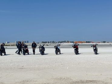 Group of people with motorcycles on a vast sandy area under a clear sky.
