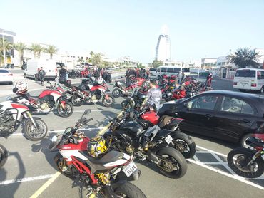 Group of motorcyclists gathered in a parking lot on a sunny day.
