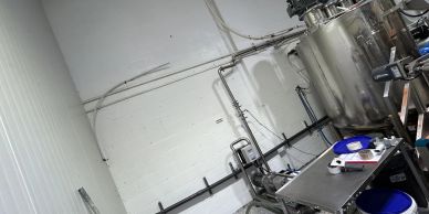 Industrial stainless steel tank and equipment by a white wall.