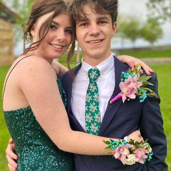 A smiling couple dressed up for a special occasion with floral accessories.