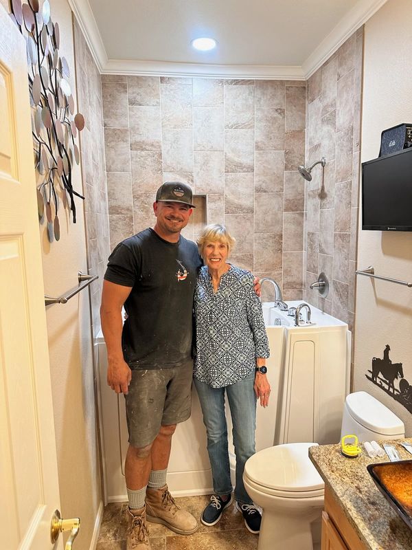 Two people smiling in a newly renovated bathroom with a walk-in tub.