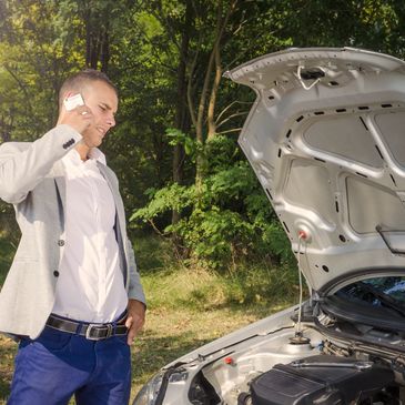 Man standing by the open hood making a phone call and trying to fix the vehicle