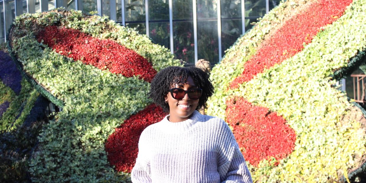 Smiling woman in sunglasses stands before a large floral butterfly.