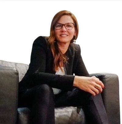 Woman in glasses sitting on a gray couch, smiling.