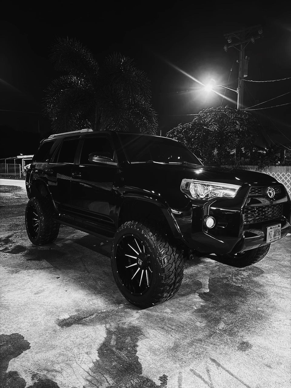 Black Toyota SUV parked under a streetlight at night with shiny wheels.