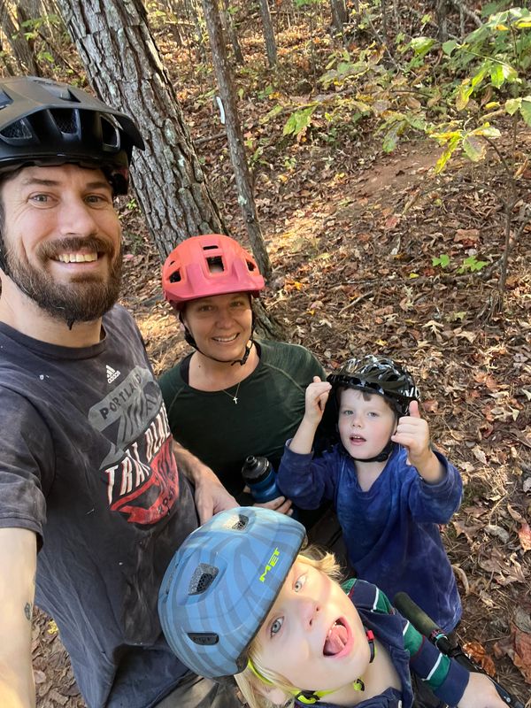 Family of four in bike helmets enjoying a forest trail.