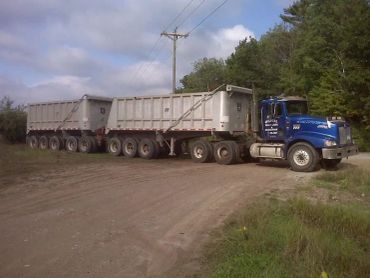 A large blue semi-truck with two trailers on a dirt road.