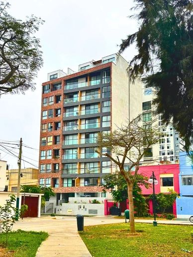 Edificio de departamentos con árboles al frente en un parque.
