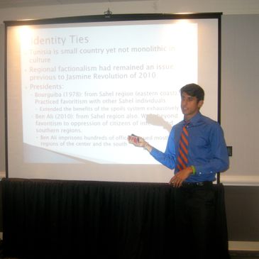 Man in blue shirt giving a presentation with projected slides.