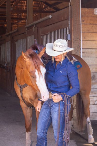 A cowgirl gently interacts with her horse in a stable.