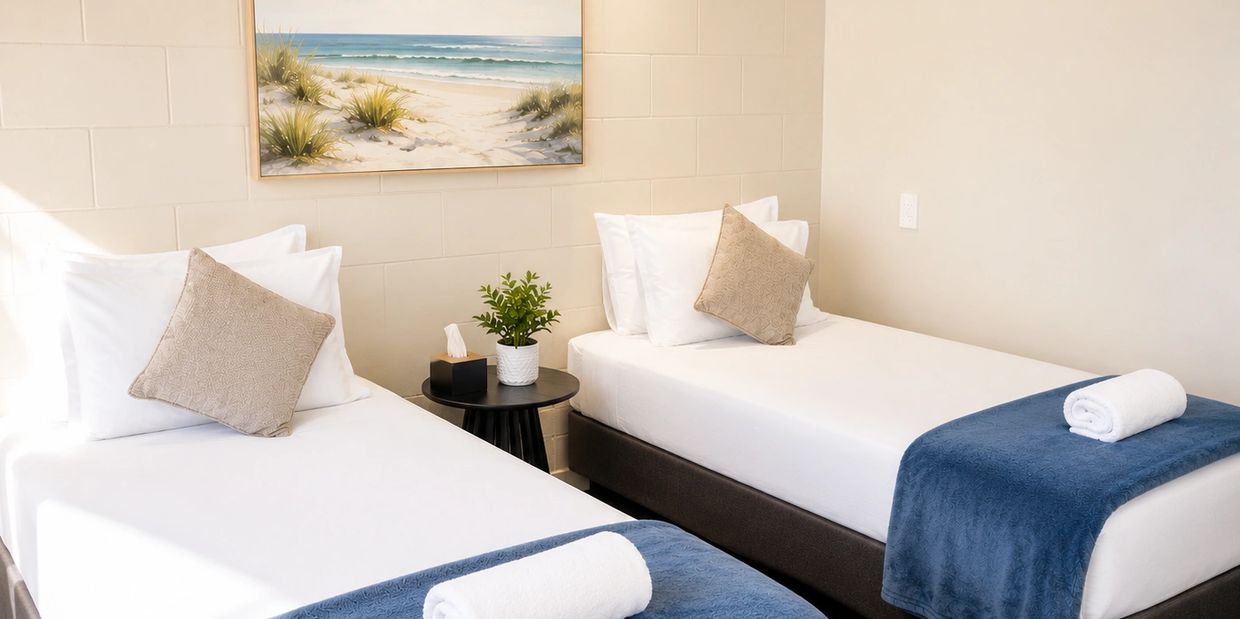 Neatly arranged twin beds with blue throws and beige cushions.