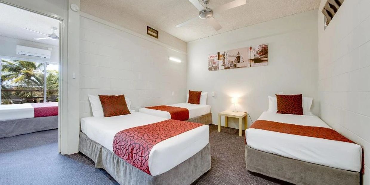 A clean room with three single beds, red accents, and a small night table with a lamp.