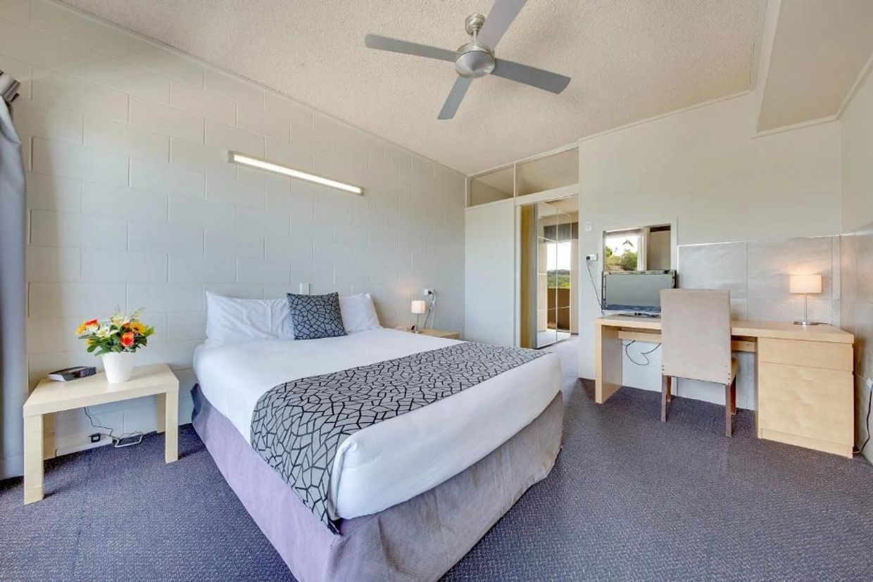 Simple, clean hotel room with a bed, desk, and ceiling fan.