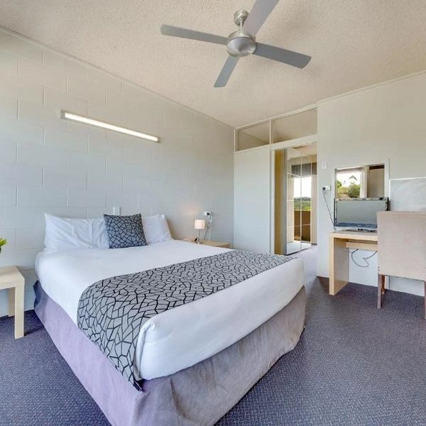 Modern hotel room with a large bed, desk, chair, and ceiling fan.