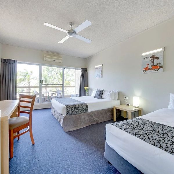 Bright hotel room with two beds, balcony, and modern amenities.